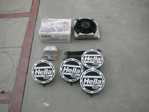1988 Ford Bronco - Collection of automotive parts including Hella lights, a radiator fan, and a Yukon branded box, laid out on a concrete surface.