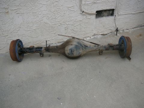 1988 Ford Bronco - Rear axle assembly with drum brakes, photographed outdoors against a textured wall.