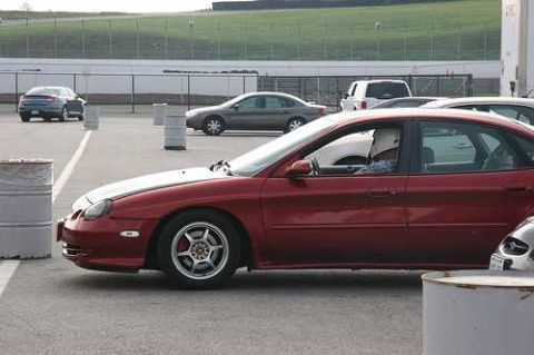 1997 Ford Taurus - A red 1997 Ford Taurus is seen from the side at a track event, with a driver wearing a racing helmet.