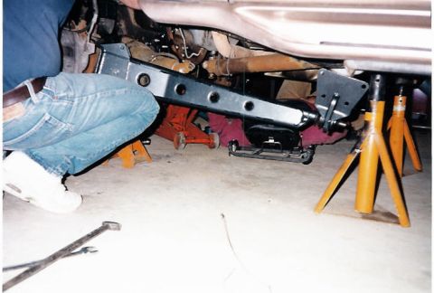 1996 Ford Bronco - Mechanic working on the undercarriage of a vehicle, installing a suspension component. The Supermotors.net logo is visible in the corner.