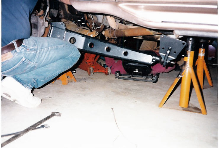 Undercarriage with black steel crossmember on yellow jack stands, person working in jeans
