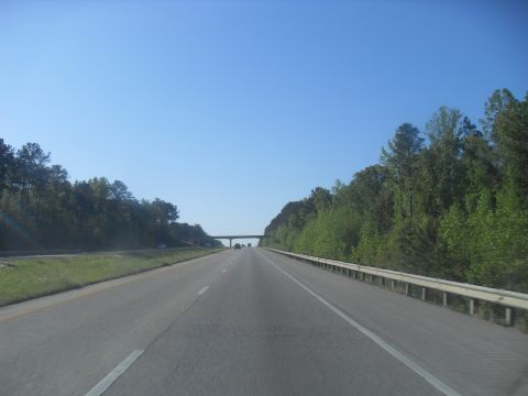 1988 Ford Bronco - A view from the road shows a clear blue sky and trees lining the highway, with a bridge visible in the distance.