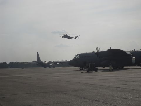 1988 Ford Bronco - Several military aircraft, including cargo planes and a helicopter, are parked on an airfield under a hazy sky.