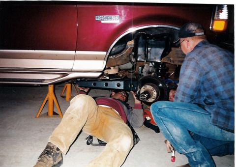 1996 Ford Bronco - Two mechanics are working on the suspension of a 1996 Ford Bronco that is raised on jack stands.