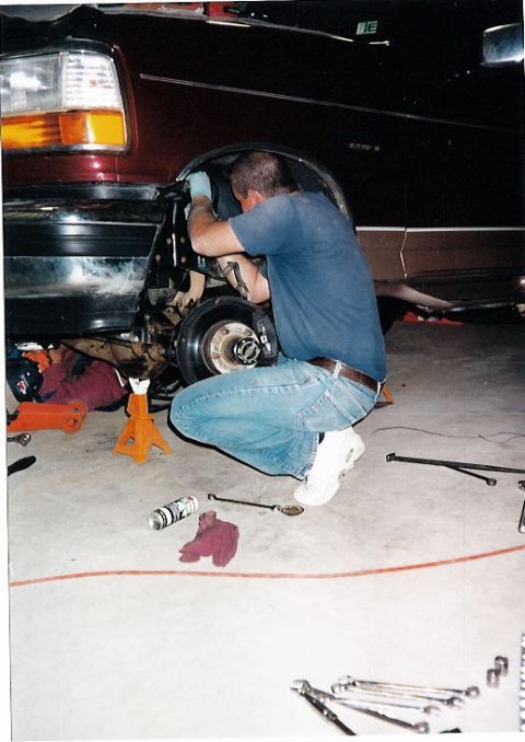1996 Ford Bronco - A person is working on the suspension of a vehicle, with tools and jack stands on the floor.