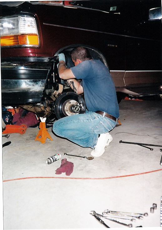 Man kneeling at front wheel hub of maroon SUV on jack stands in garage