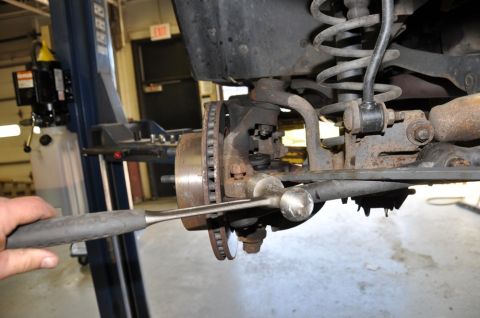 1996 Ford Bronco - Mechanic works on the suspension and brake system of a vehicle in a repair shop.