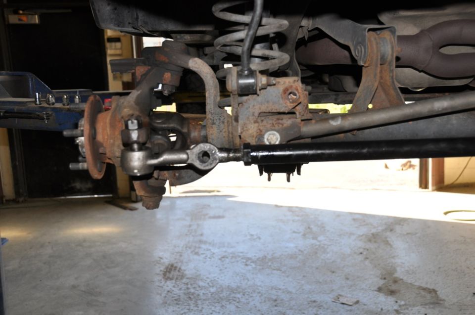 Close-up of rusty vehicle steering linkage and suspension parts, including tie rod ends and sway bar