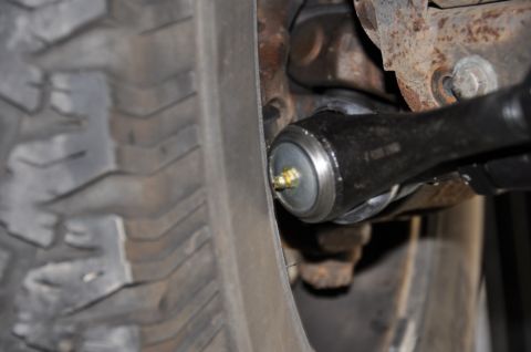1996 Ford Bronco - Close-up view of a tie rod end with a grease fitting, adjacent to a vehicle tire.