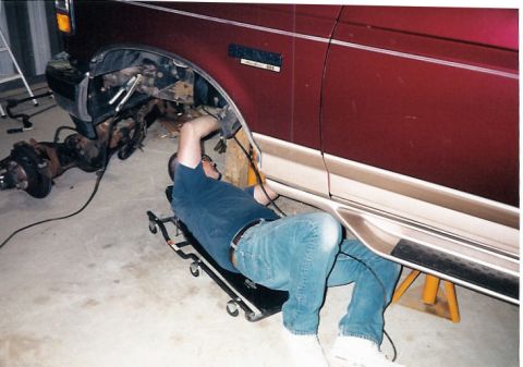 1996 Ford Bronco - A mechanic works on the suspension of a maroon 1996 Ford Bronco, with the front axle removed.
