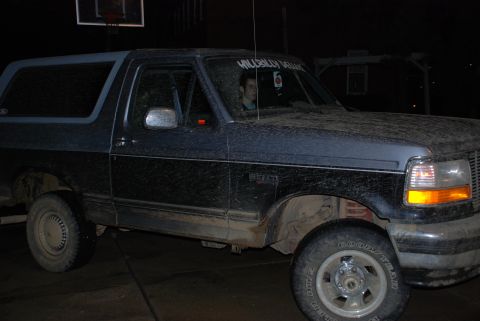 1995 Ford Bronco - A two-tone Ford Bronco is parked outside at night, covered in dirt. A person is visible in the driver's seat.
