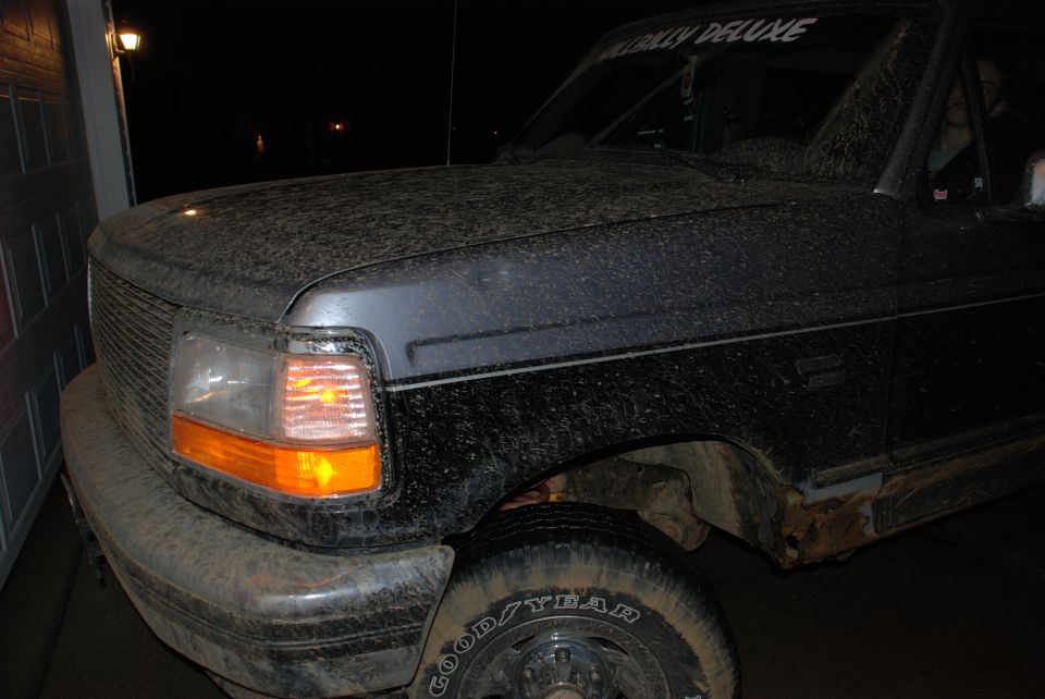 Black Ford Bronco covered in dirt, front 3/4 view, showing grille, headlight, and fender