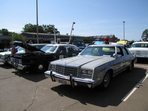 1991 Ford LTD Crown Victoria - silver Chrysler-bodied State Police sedan with a roof lightbar, lined up beside other vintage police cars at a show.