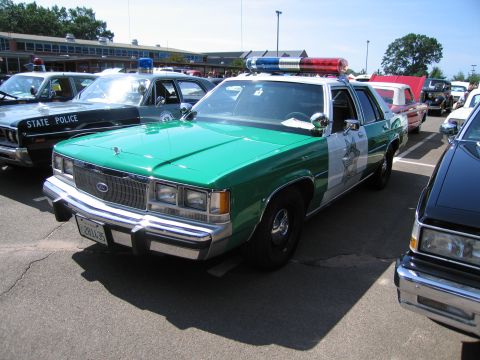 1991 Ford LTD Crown Victoria - Front three-quarter view of a green-and-white Ford LTD Crown Victoria sheriff sedan with red and blue roof lights at a car show.