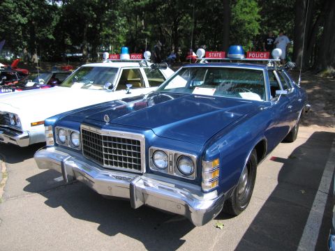 1991 Ford LTD Crown Victoria - blue Ford LTD two-door coupe parked on pavement with State Police cars and trees in the background at a show.