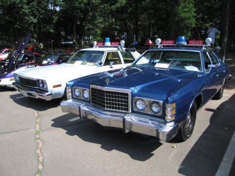 1991 Ford LTD Crown Victoria - blue Ford LTD sedan parked next to white State Police cars under trees at a car show.