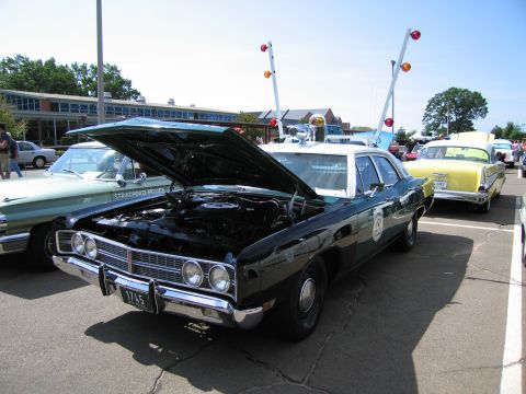 1991 Ford LTD Crown Victoria - black full-size Ford police sedan with hood raised and roof lights, parked at a car show with other vehicles around.