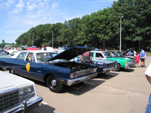 1991 Ford LTD Crown Victoria - blue full-size Dodge police sedan with its hood raised, lined up with State Police and other cruisers at a car show.