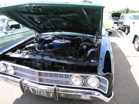 1991 Ford LTD Crown Victoria - Close view of the open engine bay and chrome front of a black classic sedan with quad headlights at a car show.