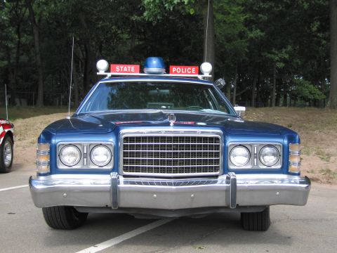 1991 Ford LTD Crown Victoria - Head-on front view of a blue 1970s Ford State Police car with chrome grille, quad round headlights and red STATE POLICE roof signs.