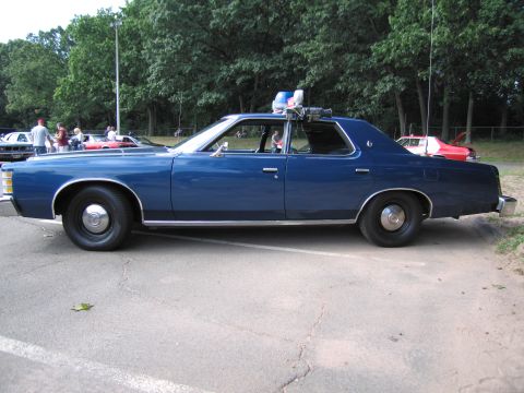 1991 Ford LTD Crown Victoria - Full driver-side profile of a blue 1970s Ford four-door State Police sedan with roof light bar, parked among show cars.