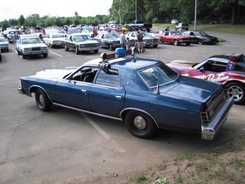 1991 Ford LTD Crown Victoria - Rear three-quarter view of a blue 1970s Ford State Police sedan with roof beacon, parked at a busy classic car show.