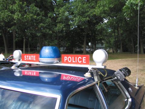 1991 Ford LTD Crown Victoria - Close-up of a police car roof bar with red STATE POLICE signs, a blue dome light, chrome spotlights and a whip antenna.