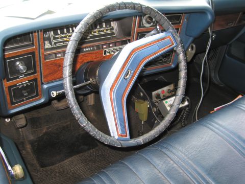 1991 Ford LTD Crown Victoria - Interior of a vintage car showing a blue dashboard with woodgrain trim, gauges, and a leather-wrapped steering wheel with a colored center…