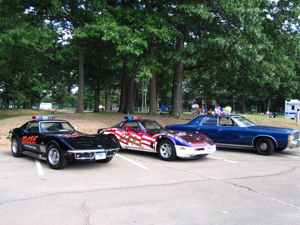 Black DARE Corvette, flag-wrapped Corvette and blue Ford sedan in a row