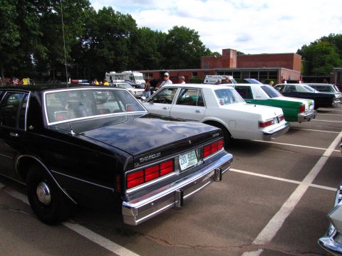 1991 Ford LTD Crown Victoria - black Chevrolet Caprice sedan shown from the rear in a parking lot car show, with a row of vintage sedans behind it.