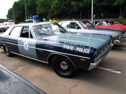 1991 Ford LTD Crown Victoria - blue-and-silver early-1970s Plymouth sedan marked STATE POLICE with a single roof beacon, parked among other classic cars.