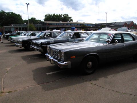 1991 Ford LTD Crown Victoria - diagonal row of gray 1970s full-size sedans, one lettered STATE POLICE, lined up at an outdoor car show.