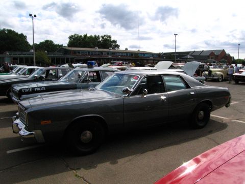 1991 Ford LTD Crown Victoria - gray 1970s Plymouth full-size sedan parked next to a black STATE POLICE cruiser at a crowded car show.