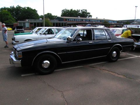 1991 Ford LTD Crown Victoria - black Chevrolet Caprice four-door sedan shown in profile among other classic cars at an outdoor show.