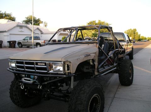 1986 Toyota Hilux - This heavily modified Toyota truck features a custom roll cage and off-road tires, with another truck visible in the background.
