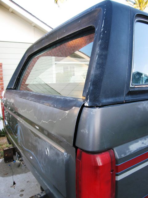 1986 Ford Bronco - The rear section of a weathered Ford Bronco shows its distinctive body style and a faded stripe along the fender.