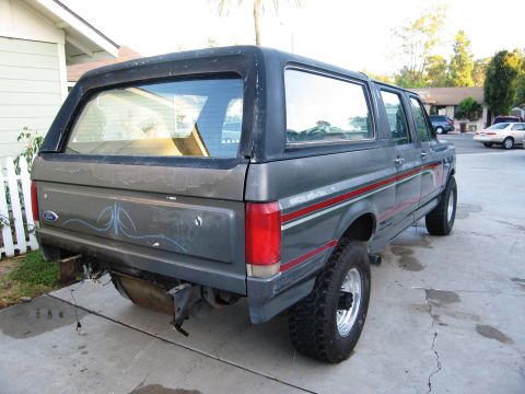 1986 Ford Bronco - Rear view of a gray Ford Bronco with custom pinstriping and aftermarket wheels, showing some paint damage.