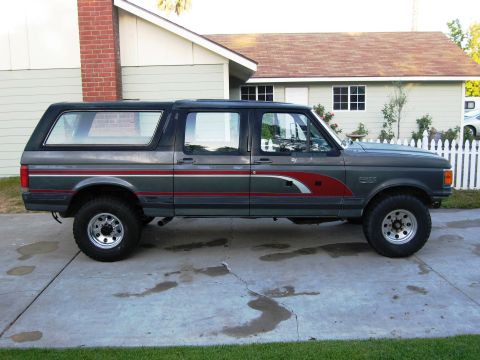 1986 Ford Bronco - Dark gray 1987 Ford Bronco SUV parked on a concrete driveway in front of a house.
