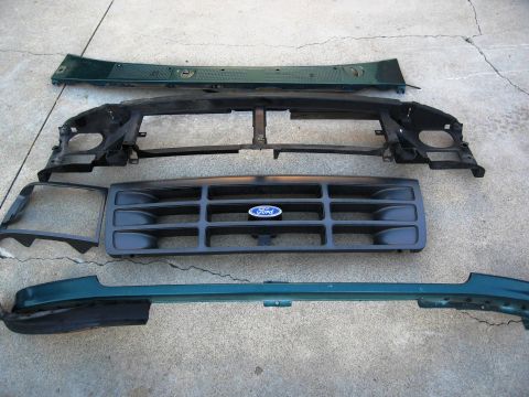 1986 Ford Bronco - Disassembled front end parts for a Ford vehicle are laid out on a concrete surface.