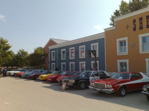 1991 Ford LTD Crown Victoria - A line of classic cars are parked in front of a western-themed building facade.
