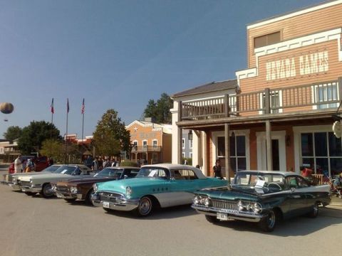 1991 Ford LTD Crown Victoria - A line of classic cars, including a green 1959 model, are parked in front of a western-themed building.
