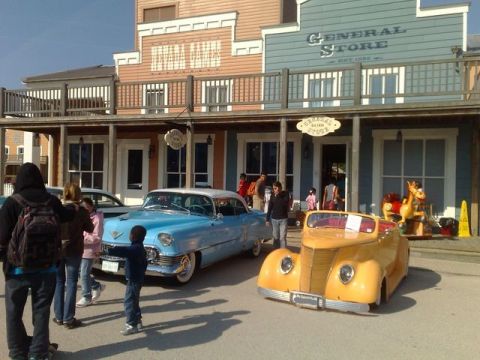 1991 Ford LTD Crown Victoria - Two classic cars are displayed in front of a western-themed building.