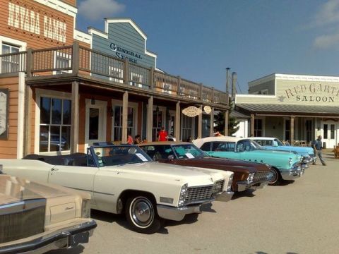 1991 Ford LTD Crown Victoria - Several classic American convertible cars are lined up in front of a general store and saloon.