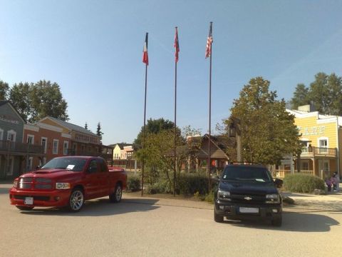 1991 Ford LTD Crown Victoria - Two trucks, a red Dodge Ram and a black Chevrolet Trailblazer, are parked outside themed buildings.