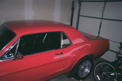 1967 Ford Mustang - Side view of a red 1967 Ford Mustang coupe with chrome trim and aftermarket wheels.