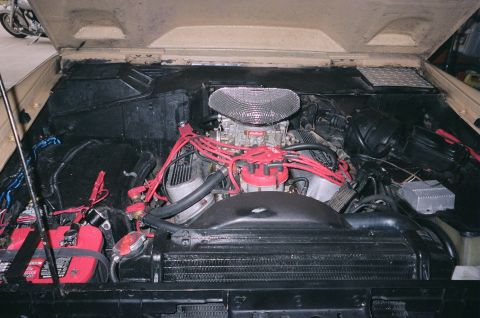 1976 Ford Bronco - The engine bay of a 1976 Ford Bronco is shown, a V8 engine with a prominent chrome air cleaner and bright red spark plug wires.