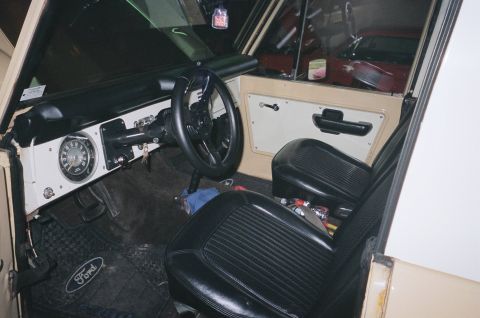 1976 Ford Bronco - The interior of a classic Ford Bronco features black vinyl seats and a tan dashboard with a prominent circular gauge.