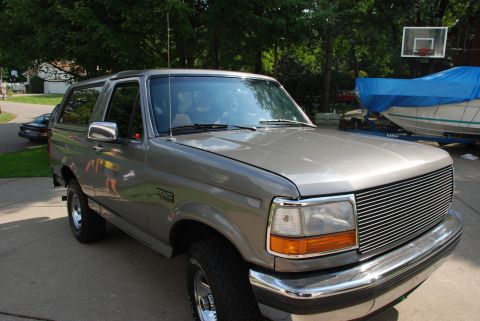 1995 Ford Bronco - This gray 1995 Ford Bronco is parked in a driveway with a boat covered in a blue tarp in the background.