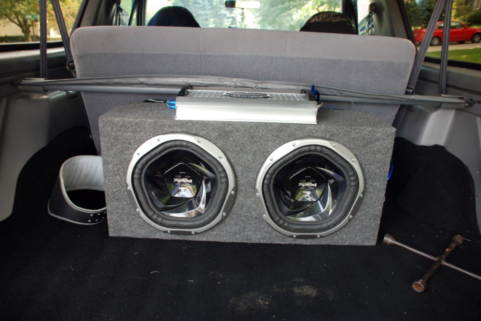 Car interior cargo area with dual subwoofers in a carpeted box and a silver amplifier mounted above