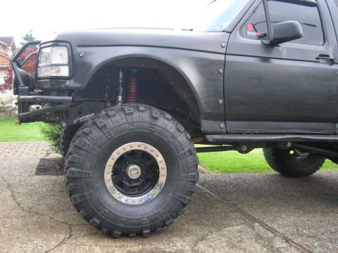 1996 Ford Bronco - Close-up front-3/4 view of a black Ford Bronco/full-size truck front corner, showing a large mud-terrain tire on a black beadlock wheel, a…